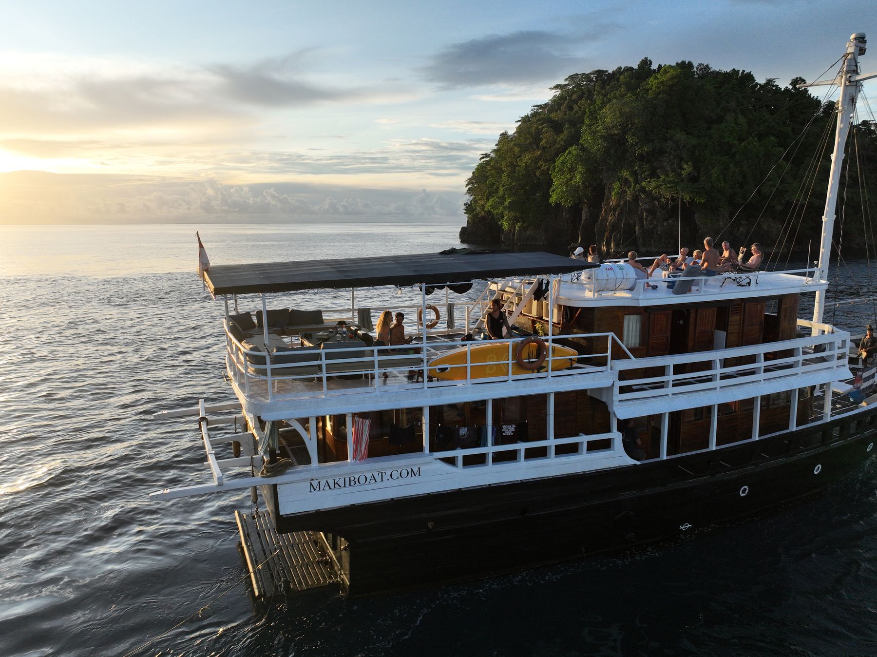 Maki at anchor, golden hour, crew on the top deck