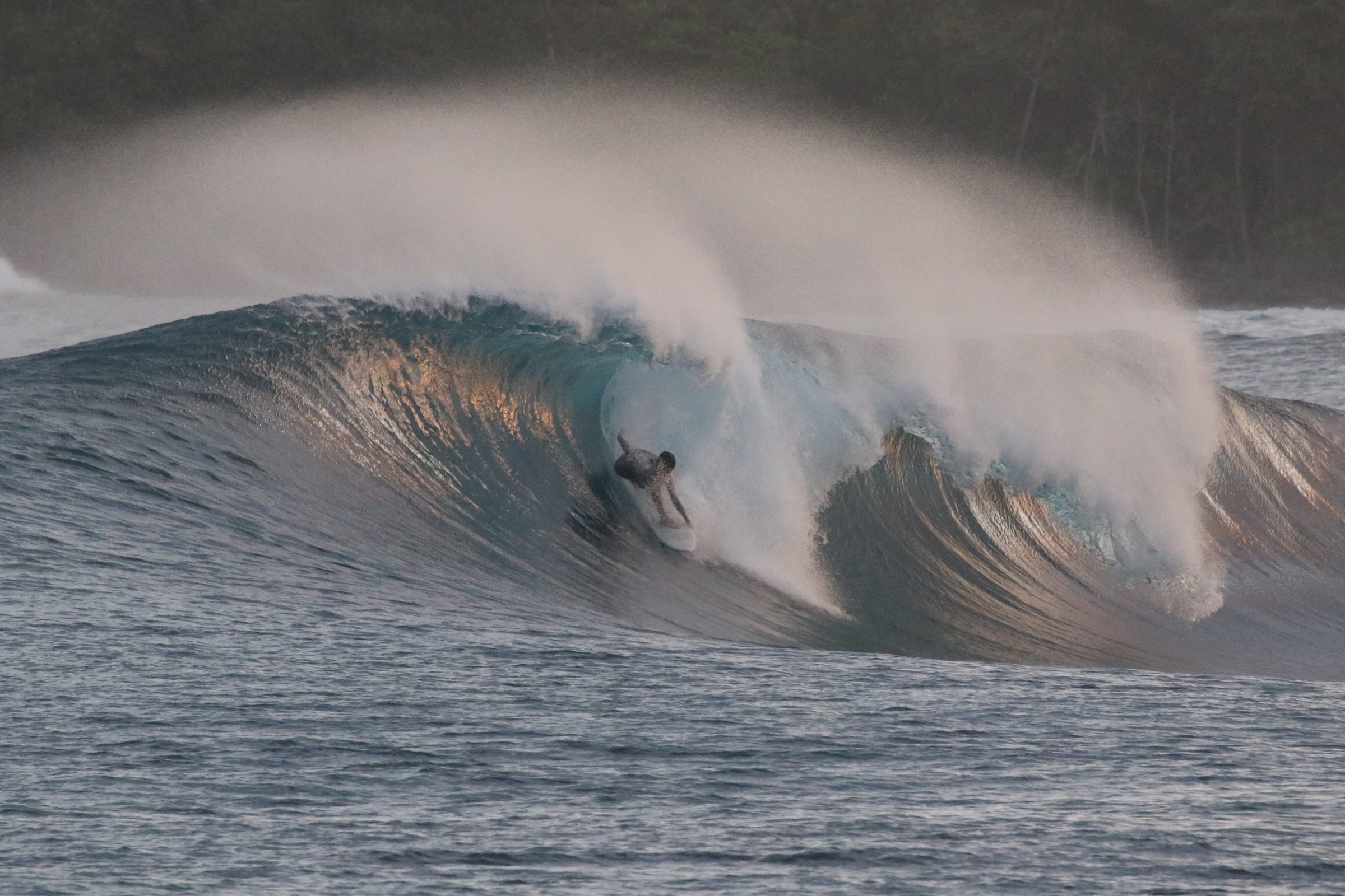 Surfer deep inside a golden-lit barrel at sunset