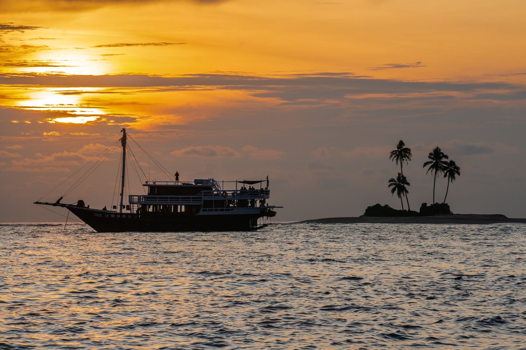 Maki at anchor beside a small palm-covered island at sunset